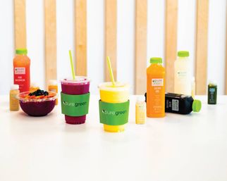 Vibrant magenta and yellow smoothies, an acai bowl, and assorted cold-pressed juice bottles displayed on a white counter in a modern health juice bar