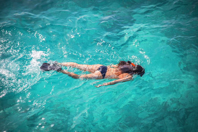 Aerial view of a snorkeler wearing fins and a snorkel floating face-down in clear turquoise tropical water