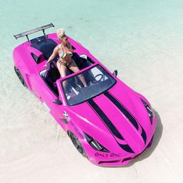 Person in a colorful bikini posing in a bright pink convertible-style beach car beached on clear turquoise water and white sand at a tropical beach