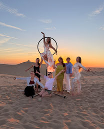 Seven women posing around an aerial hoop on sand dunes during a colorful desert sunset photoshoot