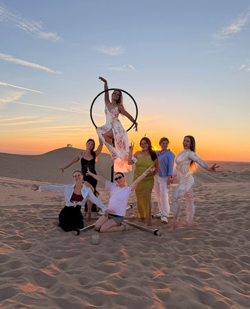 Seven women posing around an aerial hoop on sand dunes during a colorful desert sunset photoshoot