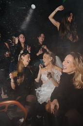 Lively nightclub bachelorette party with friends laughing, holding cocktails, and a bride-to-be in a ruffled white dress and veil under smokey disco lights
