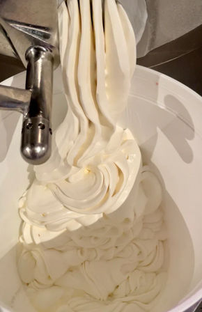 Close-up of creamy vanilla soft-serve flowing from a stainless-steel dispenser into a white bucket in a commercial kitchen