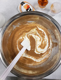 Stainless steel mixing bowl on a kitchen counter with creamy batter and pumpkin-spice swirl being stirred by a white spatula, spice jars and measuring cup nearby — cozy fall baking prep.