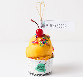 Bright yellow sorbet scoop in a confetti paper cup topped with colorful rainbow sprinkles and a shiny red cherry, close-up summer dessert photo on a white background.