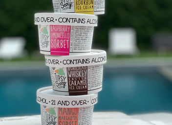 Stack of four alcohol-infused ice cream pints—raspberry limoncello sorbet, bourbon, chocolate whiskey salted caramel, and mango margarita sorbet—sitting on a poolside ledge with a blurred backyard pool in the background.
