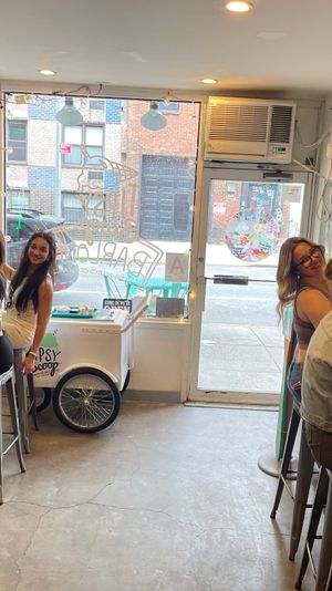 Group of friends enjoying ice cream at a cozy urban scoop shop with exposed brick wall, neon sign, metal bar stools and a street-facing window.