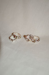 Studio product photo of silver rings on white fabric — stacked textured bands with small green and orange gemstones and sculpted wavy rings with multicolored gems.