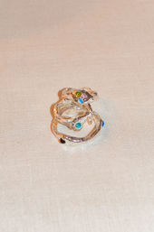 Close-up of three textured silver stackable rings dotted with colorful gemstones on beige linen — playful, organic jewelry flatlay.