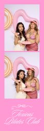 Two women in colorful bikinis pose in a pink photo‑booth strip holding a retro pink telephone, with heart-shaped and striped pool floats on a pastel backdrop for a playful summer pool-party vibe.