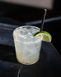 Chilled margarita-style cocktail in a short rocks glass with salted rim, ice cubes, black straw and lime wedge on a glossy bar top