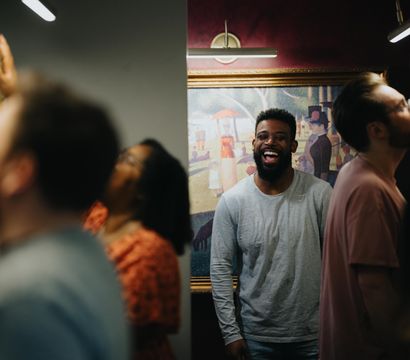 Laughing visitor enjoys art amid a busy gallery, with framed paintings on the walls and warm display lighting