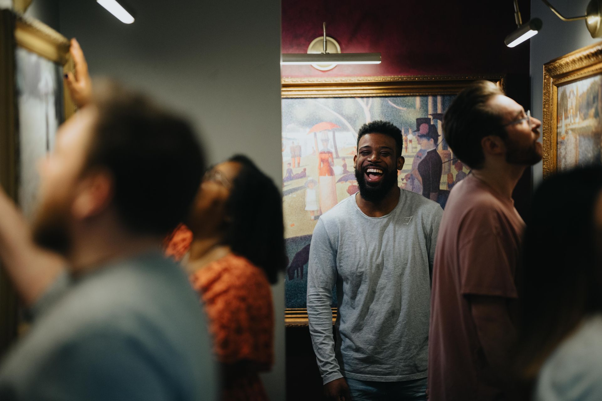Laughing visitor enjoys art amid a busy gallery, with framed paintings on the walls and warm display lighting