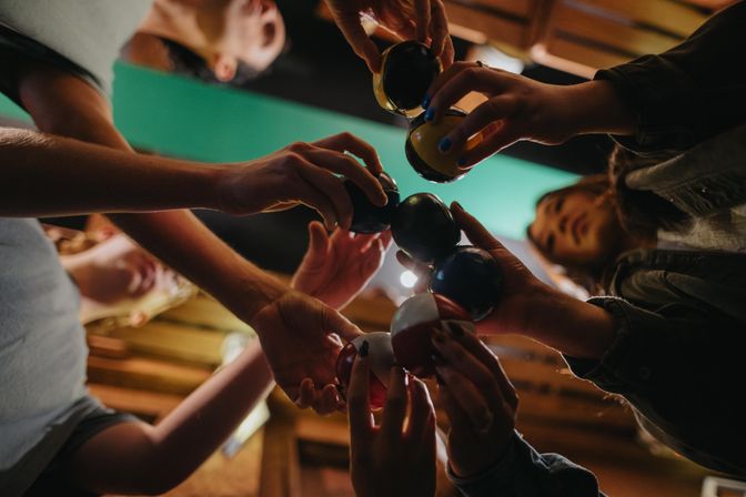 Low-angle shot of a group clinking colorful pool balls together over a table during a casual game night in a cozy billiards room.