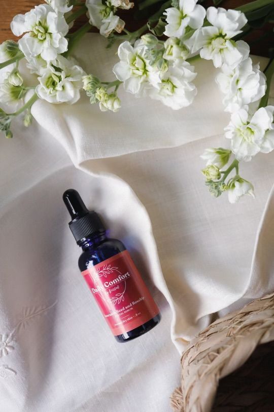 Blue glass dropper bottle of skincare serum on cream linen with white stock flowers and woven straw basket, flat lay