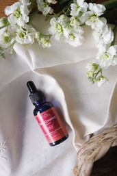 Blue glass dropper bottle of skincare serum on cream linen with white stock flowers and woven straw basket, flat lay