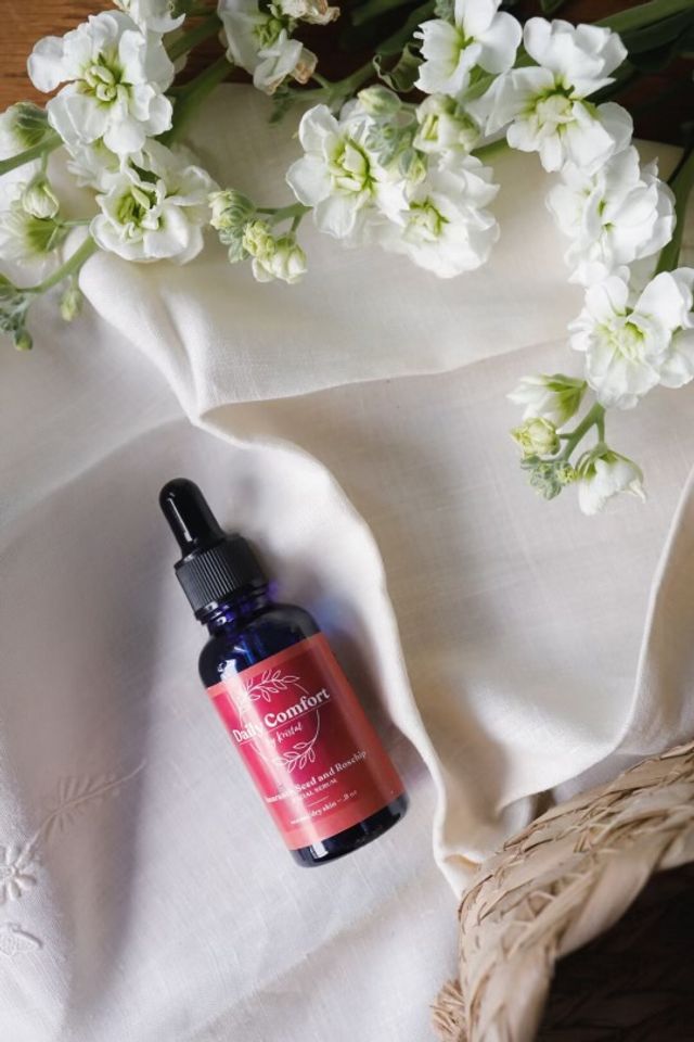 Blue glass dropper bottle of skincare serum on cream linen with white stock flowers and woven straw basket, flat lay