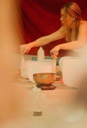 Person performing a sound bath with white crystal singing bowls and a brass singing bowl in a warm-toned meditation space