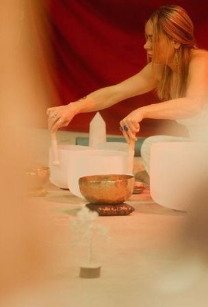 Person performing a sound bath with white crystal singing bowls and a brass singing bowl in a warm-toned meditation space