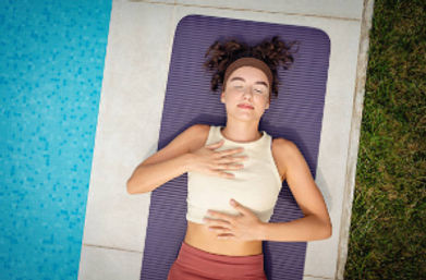 Poolside yoga: woman on a purple mat with eyes closed practicing breathwork and relaxation beside a blue swimming pool and grassy lawn.
