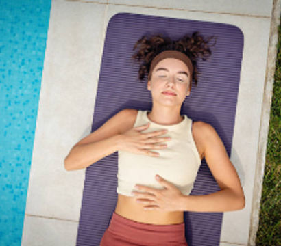 Poolside yoga: woman on a purple mat with eyes closed practicing breathwork and relaxation beside a blue swimming pool and grassy lawn.