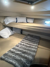 Cozy yacht cabin interior with cream leather stacked bunks, striped accent pillows, small porthole and gray faux-fur runner