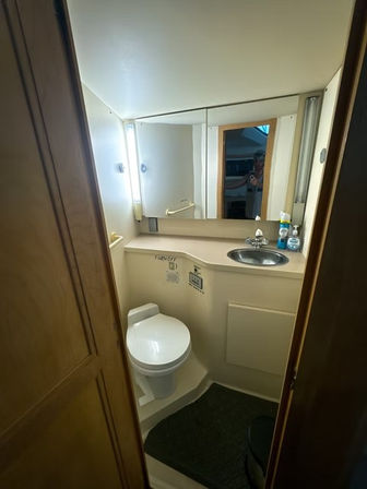 Cozy compact marine bathroom with white toilet, stainless sink set in a beige countertop, mirrored cabinet with vertical lights and small toiletries
