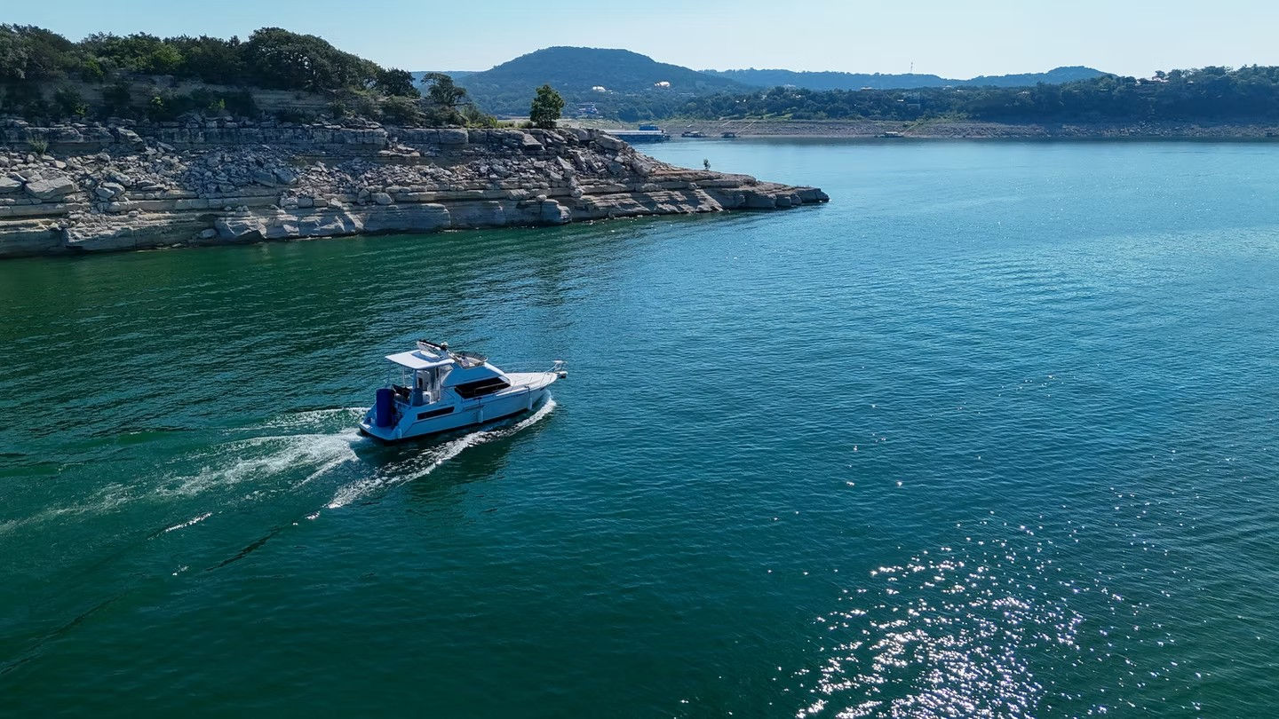 White motorboat cruising across a clear blue lake past layered limestone cliffs and tree‑topped hills under a sunny sky