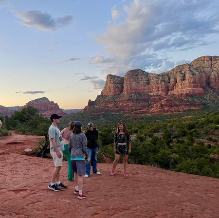 Group of people on a red rock overlook at sunset, overlooking Sedona, Arizona red sandstone buttes and green valley