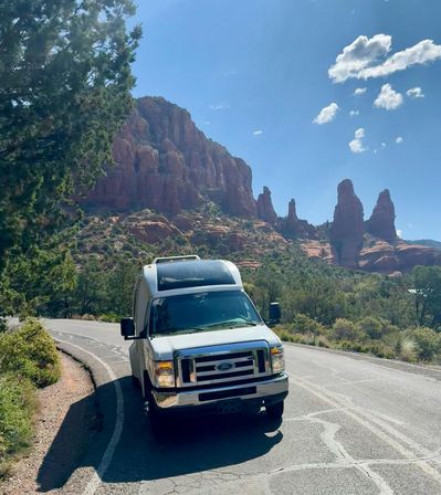 White camper van parked on a winding road with towering red rock formations and blue sky in a scenic Sedona, Arizona desert landscape