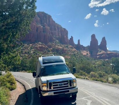 White camper van parked on a winding road with towering red rock formations and blue sky in a scenic Sedona, Arizona desert landscape