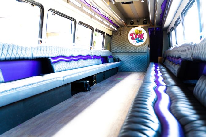 Spacious purple-accented luxury party bus interior with quilted leather bench seating, LED lighting, and wood floor