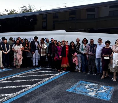 Large group of adults smiling and posing in front of a white charter coach bus in a hotel parking lot, standing across accessible parking spaces and striped pavement.