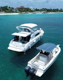 Luxury motor yacht and center-console powerboat anchored in clear turquoise water off a white-sand tropical coastline with beachfront villas.