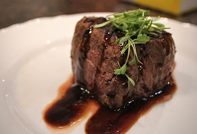 Filet mignon medallion drizzled with rich red-wine reduction and topped with microgreens on a white plate, restaurant-style plating.
