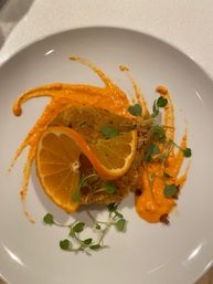 Crispy golden croquette on a white plate with a vibrant orange sauce smear, fresh orange slices and microgreen garnish — zesty plated appetizer.