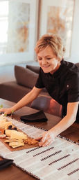 Smiling woman placing a cheese-and-cracker charcuterie board with nuts and spreads on a cozy dining room table