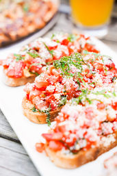 Close-up of fresh tomato bruschetta on toasted baguette slices topped with chopped basil and grated cheese on a white platter over a wooden table — Italian appetizer
