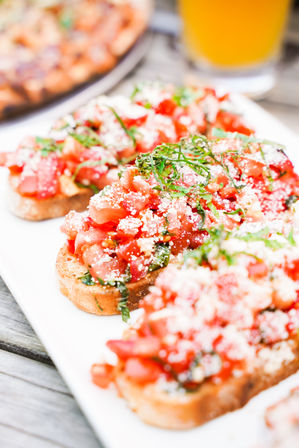 Close-up of fresh tomato bruschetta on toasted baguette slices topped with chopped basil and grated cheese on a white platter over a wooden table — Italian appetizer