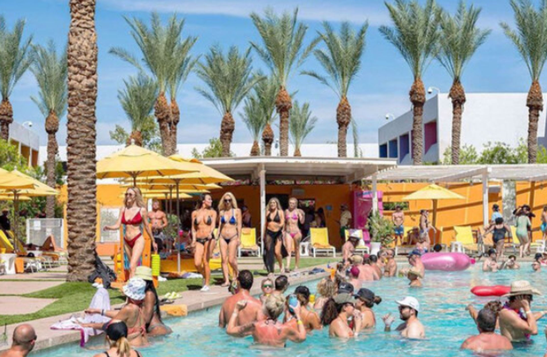 Sunny resort pool party with tall palm trees and yellow umbrellas; crowded outdoor pool with people in swimwear lounging by cabanas and socializing in the water — lively vacation scene.