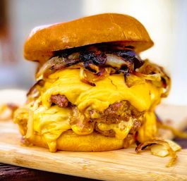 Close-up of a double juicy beef cheeseburger with gooey melted cheddar, caramelized onions and a toasted brioche bun on a wooden board