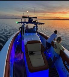 Sunset cruise on a center-console boat with glowing blue LED deck lights, people leaning on the rail as calm coastal waters reflect an orange-pink sky.