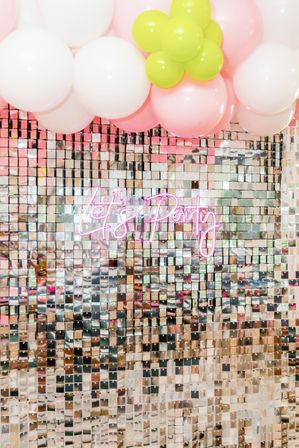 Shimmering mirrored sequin photo backdrop with a pink neon “Let’s Party” sign and pastel balloon garland in white, pink and lime green — festive party photo-op decor.