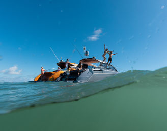 Friends jumping off a luxury yacht into turquoise ocean water on a sunny, clear-blue day with gentle waves