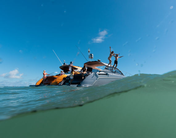 Friends jumping off a luxury yacht into turquoise ocean water on a sunny, clear-blue day with gentle waves