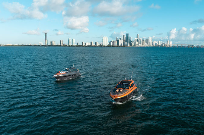 Two sleek motorboats cruising turquoise bay with Miami skyline and causeway bridge on the horizon under a sunny blue sky.