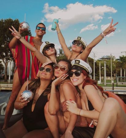 Friends at a sunny boat party by a marina, wearing captain hats, sunglasses and swimsuits, posing cheerfully