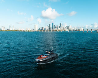 Luxury speedboat cruising through turquoise Biscayne Bay with Miami skyline and causeway bridge under a sunny blue sky