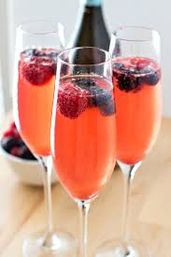 Sparkling coral-pink berry cocktails in champagne flutes garnished with raspberries and blackberries on a light wooden table — festive summer brunch drink.