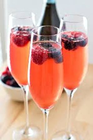 Sparkling coral-pink berry cocktails in champagne flutes garnished with raspberries and blackberries on a light wooden table — festive summer brunch drink.